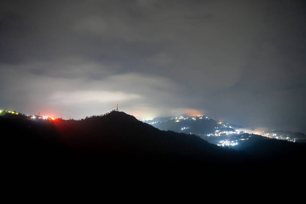 Foto notturna che mostra villaggio darjeeling immerso nel mezzo delle montagne himalaya con luci arancioni e blu in India - Foto, immagini