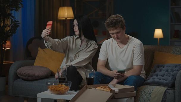 First relationships creative concept. Portrait of teenage couple spending leisure time. Boy and girl sitting on the sofa both holding smartphones, not paying attention to each other. - Фото, зображення