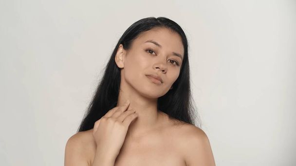 Beauty and skincare treatment creative concept. Closeup studio shot of attractive young model. Beautiful asian girl with natural makeup and long hair touching neck and looking at the camera. - Foto, Imagen