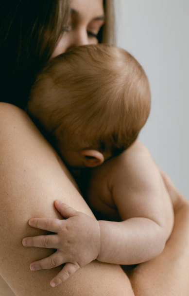 Naakte vrouw met baby in haar armen op een lichte achtergrond. Gelukkig moederschap en borstvoeding concept. Foto 's met zachte focus. Goedemorgen concept. - Foto, afbeelding