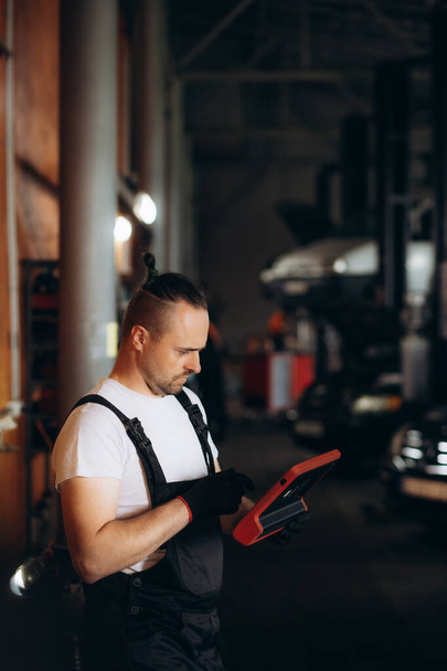Felice meccanico utilizzando tablet digitale presso officina di riparazione auto. Foto di alta qualità - Foto, immagini