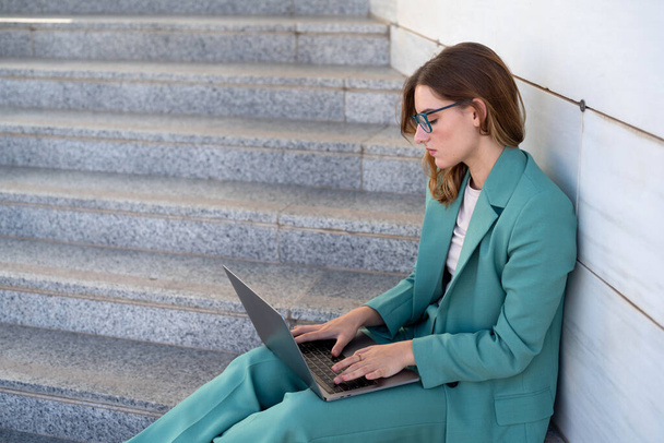 Mujer de negocios sentada en escaleras fuera del edificio de oficinas mientras trabaja con el ordenador portátil  - Foto, imagen