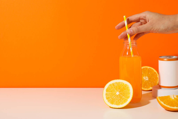 Tin can, glass bottle with juice, oranges and hand on orange background, space for text - Photo, Image