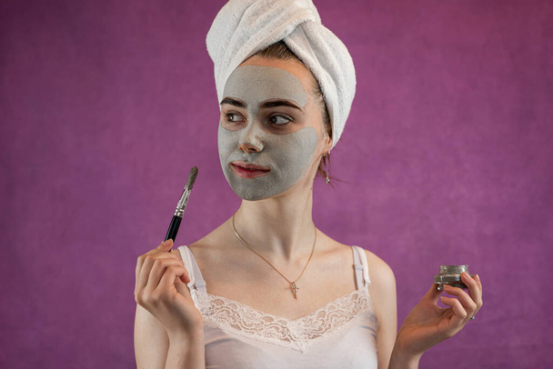 Жінка застосовує маску зеленої глини на обличчі ізольованої фіолетової, антистаріючої косметичної процедури, догляду за шкірою. - Фото, зображення