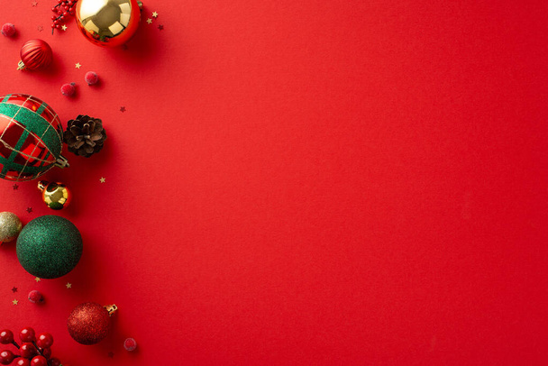Magie de Noël : Vue du haut vers le bas des décorations d'arbres festifs, des boules rouges, vertes et dorées, des accents de gui, du cône de pin, des confettis sur fond rouge, en attendant votre message spécial de vacances - Photo, image
