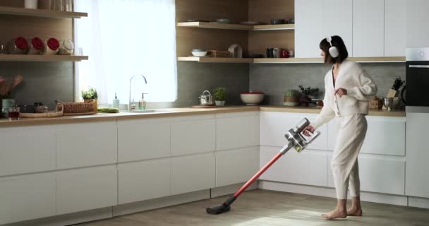 Blanke vrouw multitaken door stofzuigen en dansen in de keuken. Haar enthousiasme voor schoonmaken is duidelijk als ze grooves op de muziek, waardoor huishoudelijke klusjes een leuke en productieve activiteit. - Video