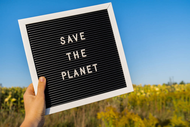 Personne méconnaissable avec un message de bannière Enregistrer la planète dans le champ de tournesol le jour ensoleillé. Signez le Jour de la Terre. Concept d'écologie et d'éco-activisme questions environnementales Arrêter le réchauffement climatique. Allez vert - Photo, image