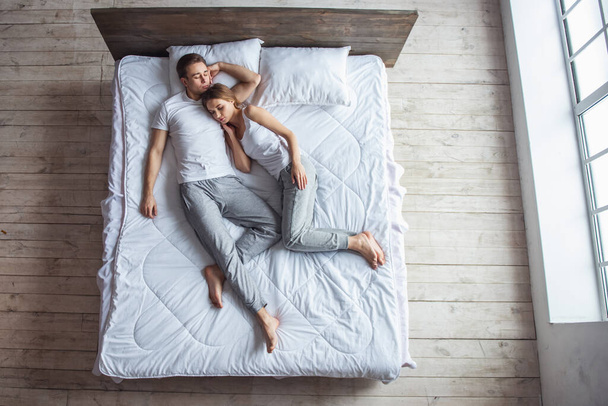 Κάτοψη του όμορφου νεαρού ζευγαριού αγκαλιάζει ενώ κοιμάται μαζί στο κρεβάτι στο σπίτι - Φωτογραφία, εικόνα