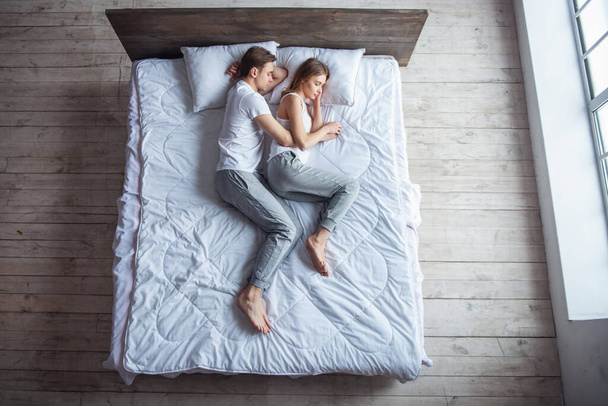 Draufsicht: Schönes junges Paar umarmt sich, während es zu Hause zusammen im Bett schläft - Foto, Bild