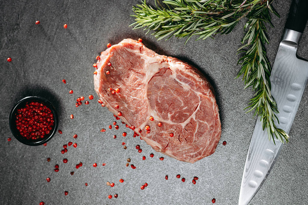 Classic fresh ribeye steak with red pepper and sprigs of rosemary on a metal plate next to a kitchen knife - Photo, Image