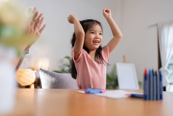 A little girl is happy to finish a draw with her mother in the living room at home. Excited mother give high five to small daughter praise child for reaching success. - Photo, Image