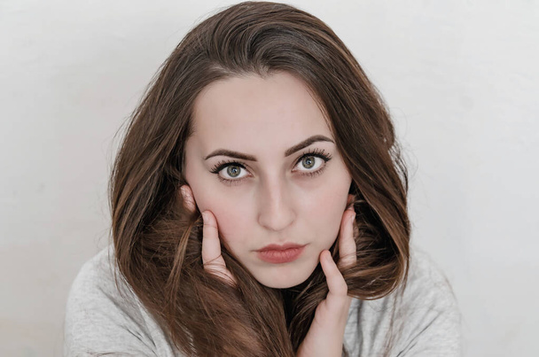 Visage féminin aux grands yeux et aux cheveux foncés. Calme expression faciale close-up. Mains près des joues - Photo, image