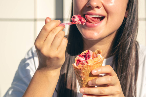 Atractiva mujer blanca alegre sonriendo ampliamente, comiendo cono de helado de bayas en la calle. - Foto, Imagen