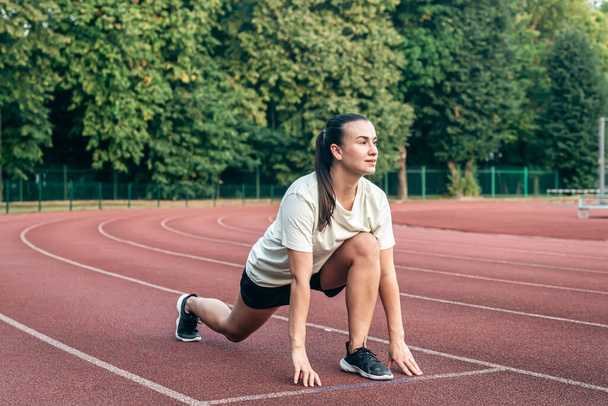 Una joven mujer caucásica en pista de atletismo se calienta y estira antes de correr. - Foto, Imagen