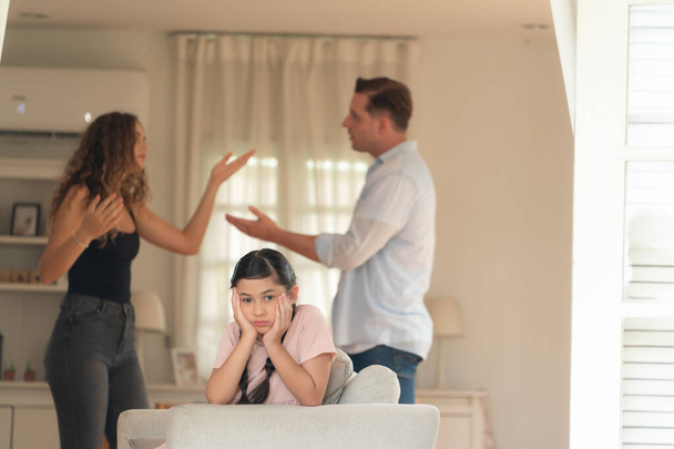 Annoyed and unhappy young girl look at camera, trapped in middle of tension by her parent argument in living room. Unhealthy domestic lifestyle and traumatic childhood develop to depression.Synchronos - Photo, Image