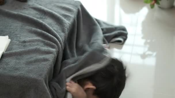 Egy ázsiai fiú bújócskázik egy takaróasztalnál a házában.. - Felvétel, videó
