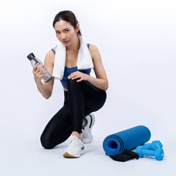 Atletik ve sportif Asyalı kadın yoğun kardiyo antrenmanından sonra dinleniyor ve su içiyor. Stüdyoda sağlıklı egzersiz ve vücut bakımına uygun yaşam tarzı takibi izole edilmiş bir arka plan. Kuvvetli - Fotoğraf, Görsel