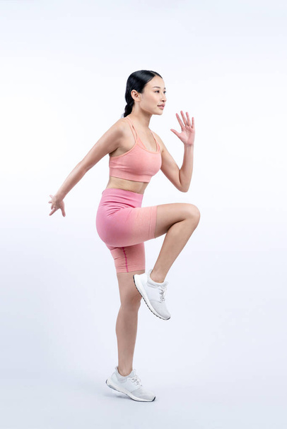Widok z boku młoda wysportowana azjatycka kobieta na bieganie postawy w studio zastrzelony na odosobnionym tle. Dążenie do zdrowego ciała dopasowanie ciała i cardio trening koncepcja stylu życia ćwiczeń. Energiczny - Zdjęcie, obraz