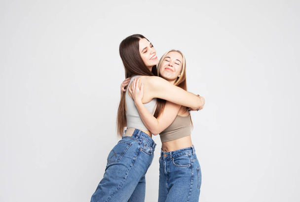 Studio shot of two happy young women friends isolated over white grey background - Foto, Imagem