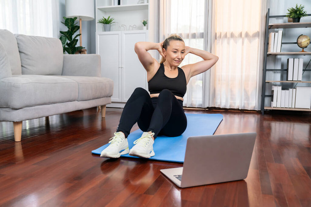 Sportovní a sportovní starší žena dělá křupání na cvičení podložky při sledování on-line cvičení doma cvičení jako koncept zdravého fit tělesného životního stylu po odchodu do důchodu. Clovek - Fotografie, Obrázek
