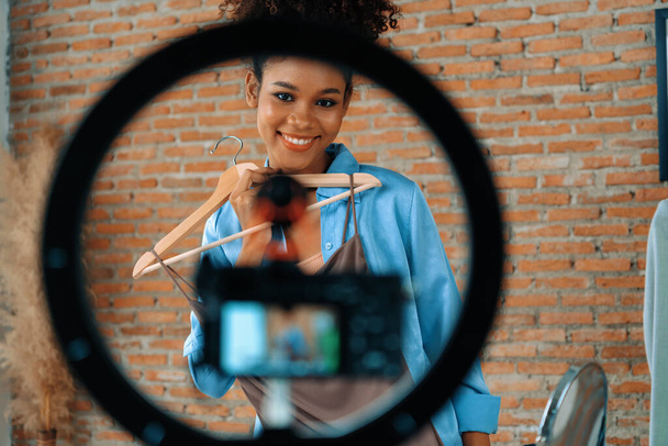 女性インフルエンサーがライブストリーミングビデオレビュー服を撮影 重要なソーシャルメディアやブログ. オンラインで録音セッション放送のためのアパレルスタジオ照明を持つ幸せな若い少女. - 写真・画像