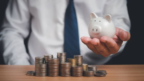Human holds a piggy bank and there are coins lined up on the wooden floor. Concepts of finance, savings, investment, and setting goals for fixed deposits with banks. - Photo, Image