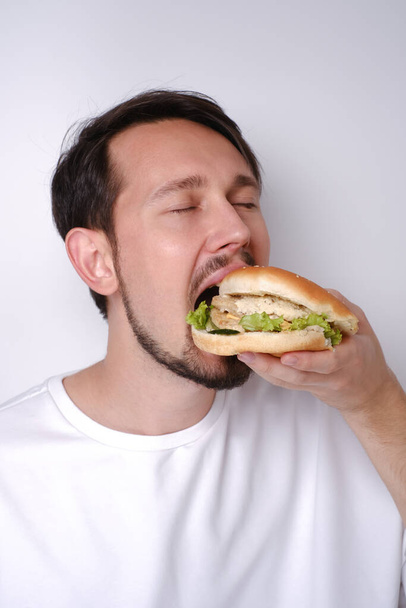 Retrato de un hombre caucásico comiendo una hamburguesa sobre un fondo blanco - Foto, imagen