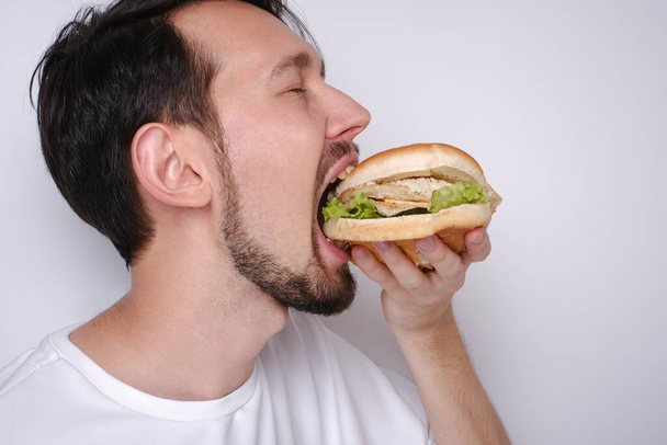 Portret van een blanke man die een hamburger eet op een witte achtergrond - Foto, afbeelding
