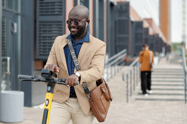 Jeune solopreneur masculin souriant en coffret choisissant les paramètres de scooter contre une employée avant de monter à la maison après le travail - Photo, image