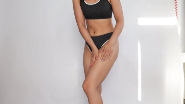 Stretch marks and cellulite on body. woman in panties applying moisturising body cream on her legs, using anti-cellulite lotion or sunscreen while standing on white background, cropped. - Footage, Video