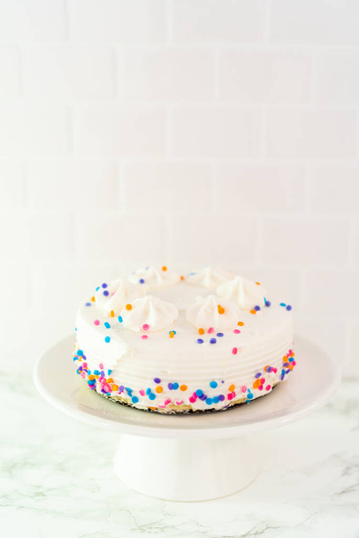 Pequeño pastel de cumpleaños blanco con funfetti espolvorea en un plato de pastel blanco. - Foto, Imagen