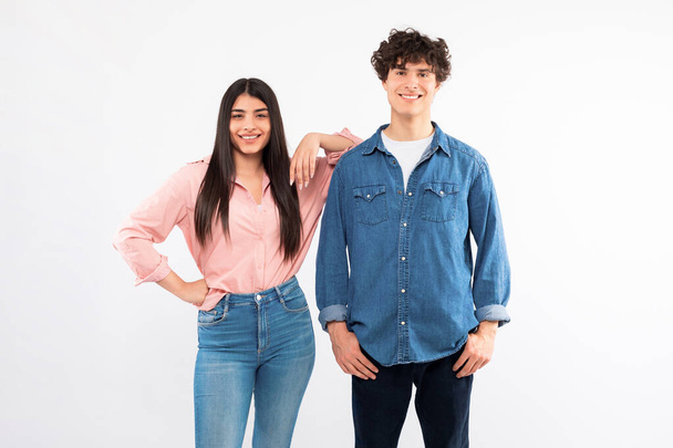Shot Of Happy Young Couple Over White Studio Background, Brunette Girlfriend Leaning On Boyfriends Shoulder Posing Together. Young People, Friendship And Romantic Relationship - Photo, Image