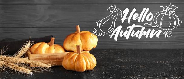 Banner with text HELLO AUTUMN and pumpkin shaped buns on dark table - Photo, Image