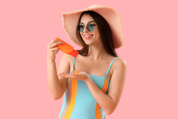 Mujer joven aplicando crema protector solar sobre fondo rosa - Foto, Imagen