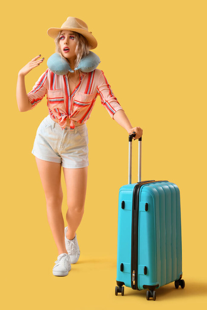 Young woman with neck pillow and suitcase on yellow background - Photo, Image