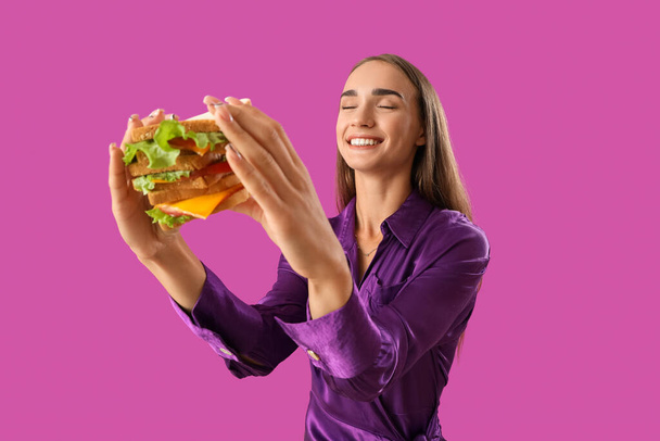 Schöne junge Frau mit leckerem Sandwich auf lila Hintergrund - Foto, Bild