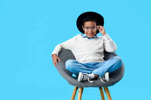 アフリカ系アメリカ人の少年が青い背景にアームチェアに座る - 写真・画像