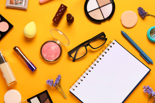 Makyaj malzemeleri, gözlükler, güzel çiçekler ve turuncu arka planda not defteri. - Fotoğraf, Görsel