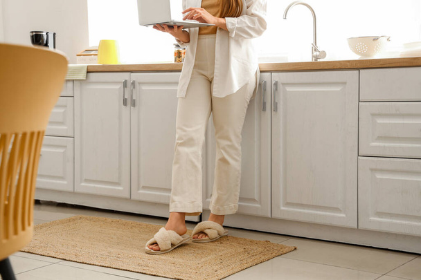 Woman using laptop on wicker carpet in light kitchen - Photo, image