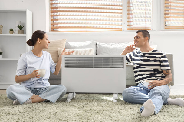 Young couple with tea warming near radiator at home - Photo, Image