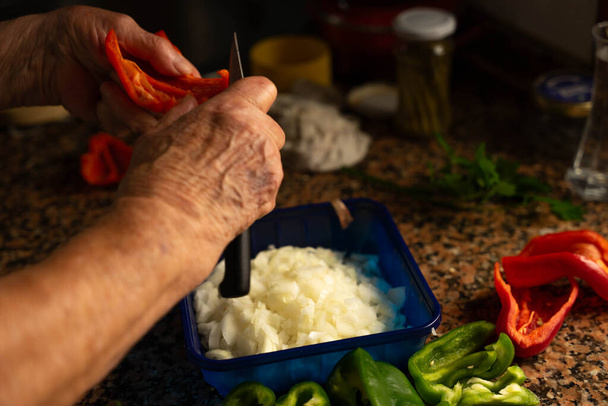 Руки с ножом и пименто, чтобы нарезать последний, который сопровождает лук при приготовлении пищи - Фото, изображение