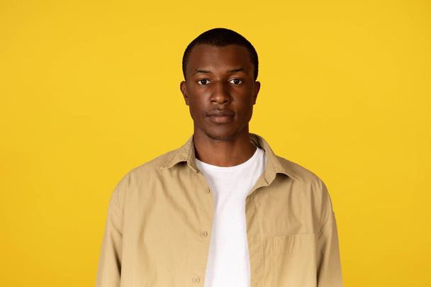 Portrait of serious calm young african american guy in casual looking at camera, isolated on yellow studio background. Headshot at video call, study and work, ad and offer, facial expression - Photo, Image