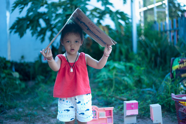 Розумна дівчина грає з коробкою і тримає шматочки паперу над головою як дах. - Фото, зображення