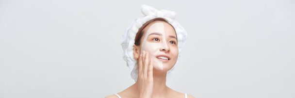 Ευτυχισμένη γυναίκα με μια πετσέτα στο κεφάλι εφαρμόζει μια μάσκα καθαρισμού στο πρόσωπό της. Μπάνερ  - Φωτογραφία, εικόνα