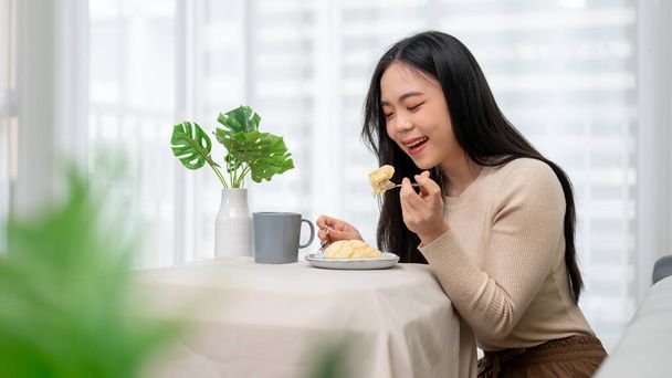 Красива і весела молода азіатка насолоджується сніданком за обіднім столом вдома. Люди та харчові концепції - Фото, зображення