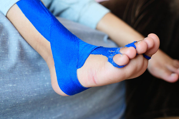 Elastisches therapeutisches blaues Klebeband, das auf das Bein des Kindes aufgetragen wird. Kinesio Taping-Therapie bei Verletzungen. - Foto, Bild