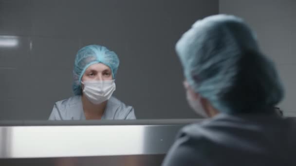 Az egyenruhás sebész megtisztítja a kezét műtét előtt, és tükörbe néz. Női nővér készül elvégezni műtéti műtét súlyos sérült beteg. A szanitéc az egészségügyi intézményben dolgozik. Visszanézés. - Felvétel, videó