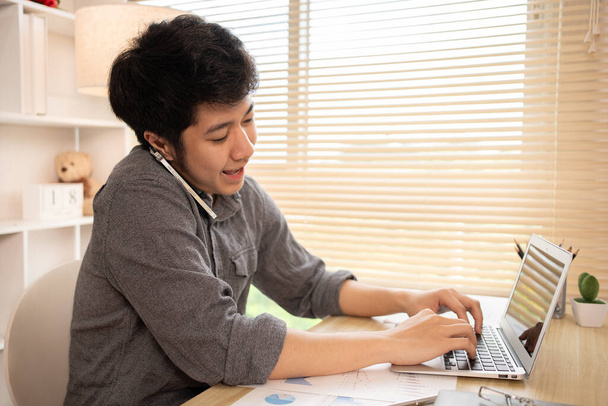 Junger Mann Multitasking: Tippen am Laptop und Telefonieren im Home Office, Home Workspace, Junger Mann, der viel Arbeit hat und sehr beschäftigt ist. - Foto, Bild