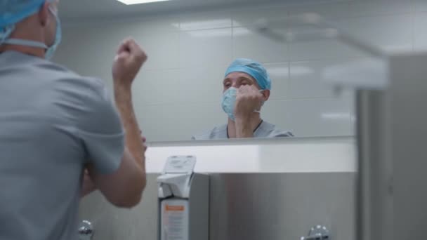 Хірург в уніформі чистить руки з милом перед операцією. Чоловічий лікар готується до хірургічної операції з важко пораненим пацієнтом. Медичний персонал працює в сучасній лікарні. Вид ззаду. - Кадри, відео