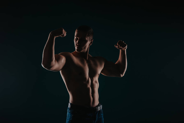 Silueta fotografie silného muže, jak ukazuje biceps a hrdě se na ně dívá. Koncept sportovní motivace - Fotografie, Obrázek
